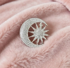 Detailed view of silver moon and star brooch with sparkling crystals on pink plush