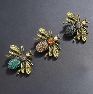 Vintage gold bee brooches with colorful rhinestones on a charcoal textured surface