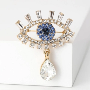 Macro shot of gold evil eye brooch with blue crystals and a teardrop crystal pendant