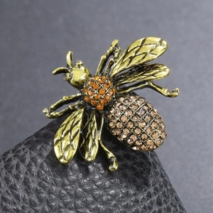 Vintage gold bee brooch with orange rhinestones on a black leather display base