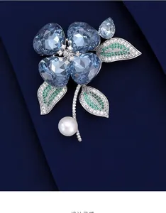 Détail macro d'une broche orchidée avec cristaux de cœur bleus, feuilles pavées et perle