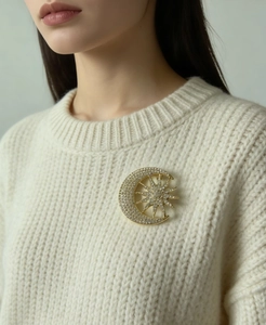 Detailed close-up of a sparkling gold star and moon brooch pinned on a white knit sweater