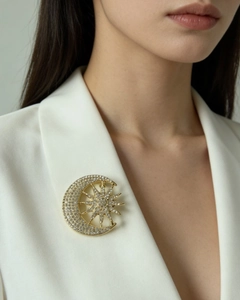Detail of a gold sun and moon brooch with crystals pinned on a white blazer lapel