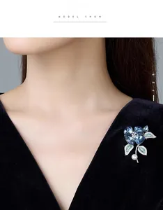 Gros plan d'une élégante broche orchidée en cristal bleu avec feuilles vertes et perle blanche