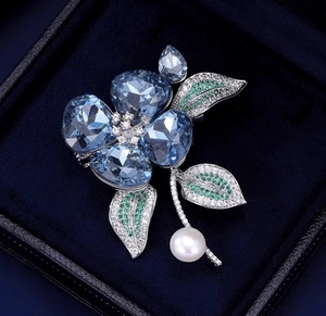 Détail d'une broche fleur en cristal bleu avec pierres d'émeraude et perle sur velours