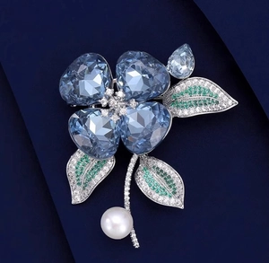 Gros plan détaillé d'une broche fleur en cristal bleu avec feuilles vertes et perle