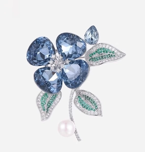 Détail de la broche fleur avec pétales en cristal bleu, feuilles vertes et perle blanche