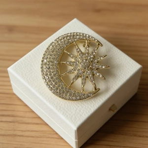 Elegant gold celestial brooch with moon and star crystals on white jewelry box