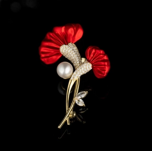 Elegante rote Blumenbrosche mit weißer Perle und Goldmetall auf schwarzem Hintergrund