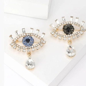 Luxury Evil Eye brooches with blue crystals and teardrop pendant on minimalist white display