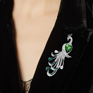 Elegant silver peacock brooch with green gemstones and white diamonds on black velvet