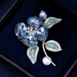 Broche orchidée en cristal bleu avec perle blanche sur un coffret en velours bleu