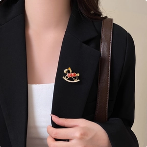 Elegant gold hollow rocking horse brooch with red enamel and pavé crystals on a black blazer