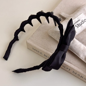 Elegant black satin bow headband with inner teeth for volume, placed on decorative books