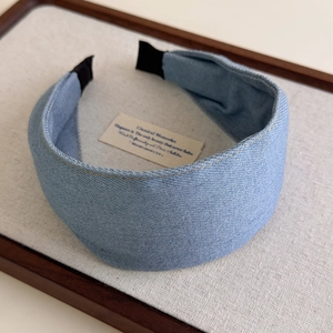 Detailed view of light blue denim wide headband with yellow stitching and black ends