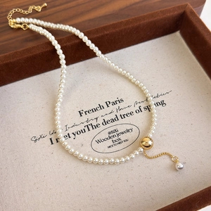 Detailed close-up of a minimalist pearl necklace with a brushed gold sphere in a box