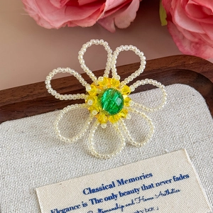 Dettaglio charm floreale fatto a mano con perle bianche e cristallo centrale verde