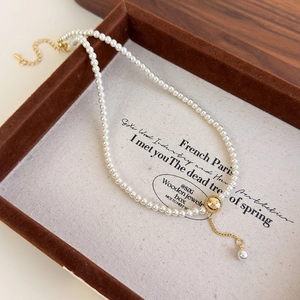 Detail of pearl necklace featuring a brushed gold ball pendant and delicate pearl tassel