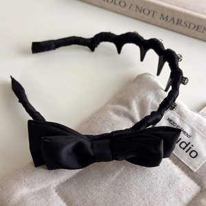Detail of black satin bow headband with wavy comb teeth and sparkling rhinestone accents