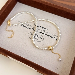 Detailed macro of pearl necklace featuring brushed gold bead and delicate tassel pendant