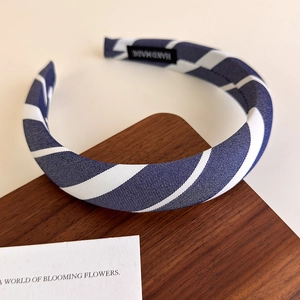 Close-up of blue and white striped padded headband with handmade label on wooden base
