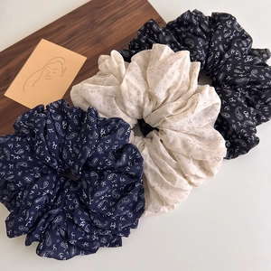 Three oversized paisley print scrunchies in navy, cream, and black on a wooden tray