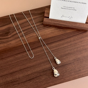 Minimalist silver Y-shaped necklace with double teardrop pendants on dark wood surface