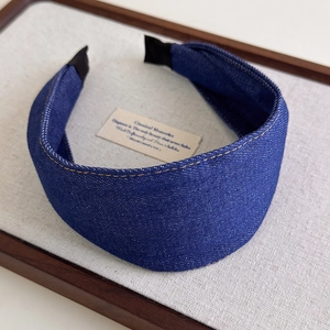 Detailed shot of dark blue denim headband with yellow stitching on linen display