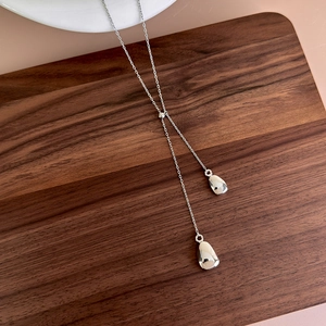 Detail of silver Y-shaped necklace with teardrop pendants on a wooden background