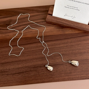 Detailed close-up of adjustable silver teardrop necklace on a dark walnut wood surface