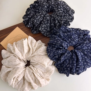 Detailed macro view of large paisley print fabric scrunchies in navy, black and cream colors