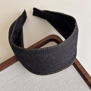 Detail of wide denim headband with orange contrast stitching and woven texture