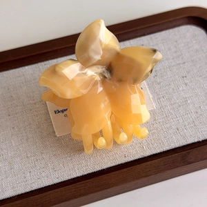 Detail view of amber floral hair claw clip with marble texture on wooden tray