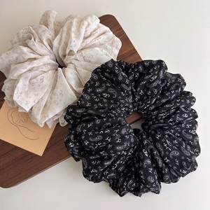 Detail of beige and black paisley scrunchies set on a wooden tray with artistic card