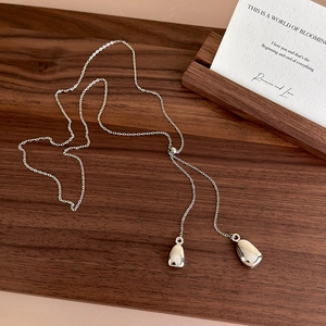 Detailed close-up of a silver teardrop Y-necklace on a walnut wood surface with fine luster