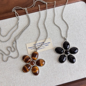 Vue détaillée de colliers pendentifs fleurs avec pierres œil de chat et résine noire