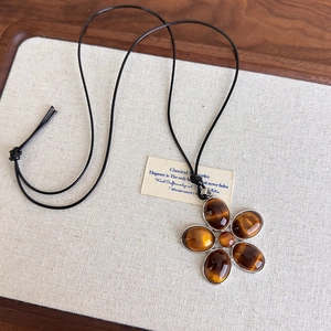 Détail du pendentif fleur en résine œil de tigre avec cordon noir sur présentoir en lin