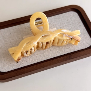 Macro detail of amber marbled large hair claw clip with twisted design on wood tray