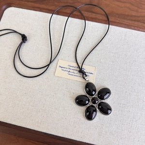 Détail d'un pendentif fleur en résine vintage avec pétales noirs et bordure argentée