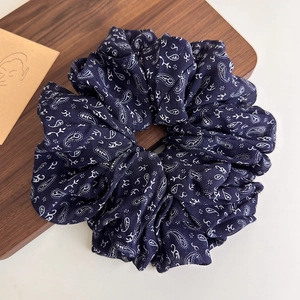Close-up of oversized navy blue paisley chiffon scrunchie on dark wooden tray