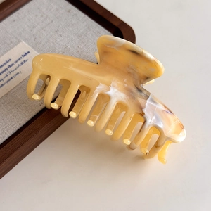 Detailed view of an amber-textured acetate hair claw clip on a luxury display tray