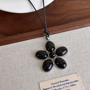 Gros plan du collier pendentif fleur en résine noire avec bords argentés sur cordon