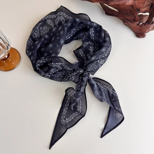 Detailed view of black paisley cotton-linen scarf tied in a stylish knot on cream background