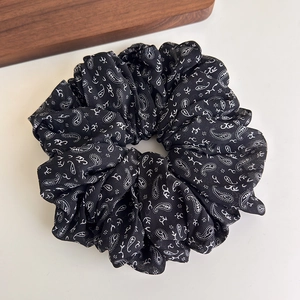 Macro shot of black paisley silk scrunchie with intricate patterns on a wooden tray
