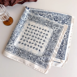 Detail view of square silk scarf with navy paisley print and satin finish on white fabric