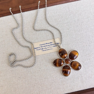 Gros plan d'un pendentif fleur en résine rétro sur un collier à chaîne à billes