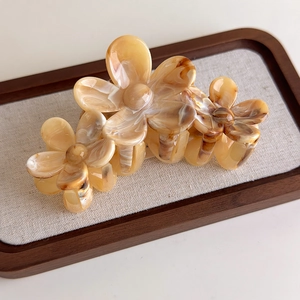 Detail view of floral tortoiseshell hair claw clip with amber resin texture on linen tray