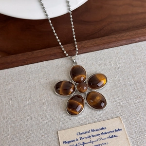 Détail du pendentif fleur rétro avec pierres effet œil de tigre sur une chaîne à boules