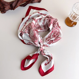 Detail view of square silk scarf featuring red paisley patterns and premium red rolled edges