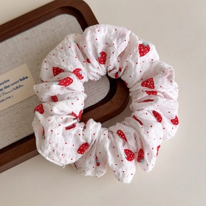 Detaillierte Makroaufnahme von weißem Scrunchie mit Erdbeermuster auf einem Holztablett